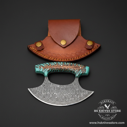 Raindrop Damascus steel ulu knife with pine cone teal resin handle and tan crescent leather sheath on dark charcoal background studio shot