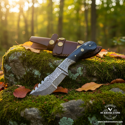 Damascus steel gut hook knife with bone handle and dark brown leather sheath on mossy rocks in forest setting