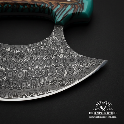 Close-up macro of raindrop Damascus steel ulu knife blade showing bold teardrop oval Damascus pattern and open thumb hole and polished curved edge