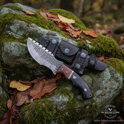 Damascus steel tracker knife buffalo horn handle resting on mossy rocks in outdoor forest setting clear blade visible