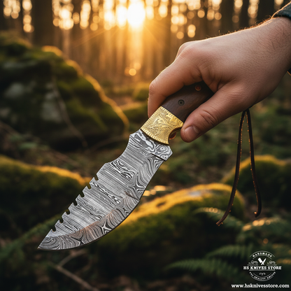 Hand gripping dark wood handle Damascus tracker knife with engraved brass bolster in outdoor forest action shot