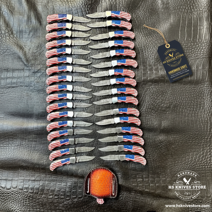 35 Damascus pocket knives USA flag handles herringbone fan pattern flat lay with HS Knives Store hang tag on dark crocodile leather