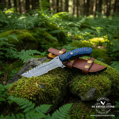 Damascus tracker knife with blue pakkawood handle and tan leather sheath placed on mossy rocks in forest outdoor setting