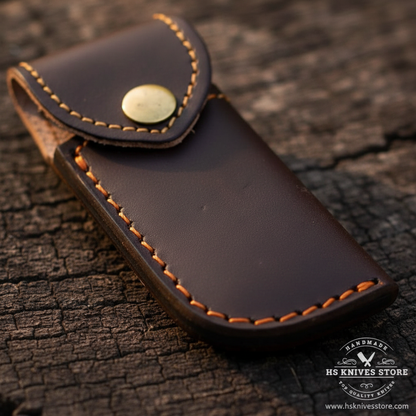 Close-up macro of dark chocolate brown leather sheath with orange amber stitching and brass snap button closure