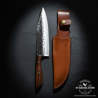 Carbon steel chef knife displayed vertically on dark slate with walnut wood handle and tan leather sheath luxury shot