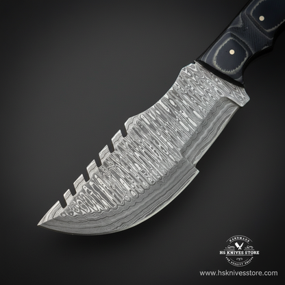 Close-up of Damascus steel tracker knife blade showing layered wavy pattern and serrated spine finger grooves