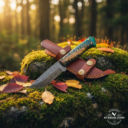 Damascus steel skinner knife with green resin pine cone handle and tan leather belt sheath on mossy rocks in forest setting