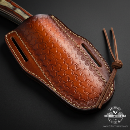 A close-up of a brown leather knife sheath with an embossed scale pattern, contrast stitching, and a leather lanyard, shown on a dark background with an HS Knives Store watermark.